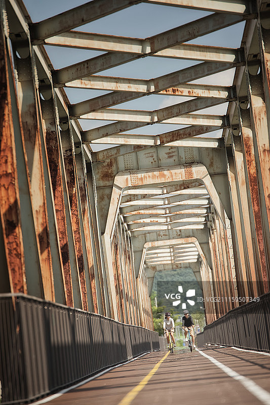 情侣戴着头盔骑自行车经过桥的摄影照片图片素材