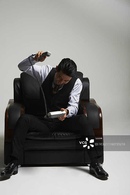 男子穿西装坐在沙发上生气地打电话的摄影作品图片素材