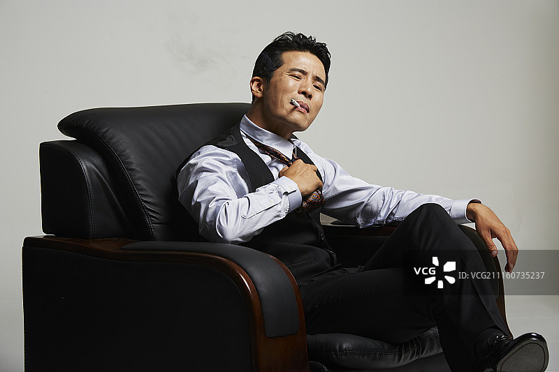 男人穿西装坐在沙发上吸烟的照片图片素材
