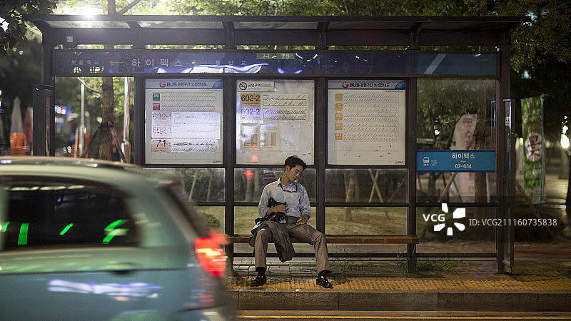 商人坐在夜间巴士站长椅上的摄影作品图片素材