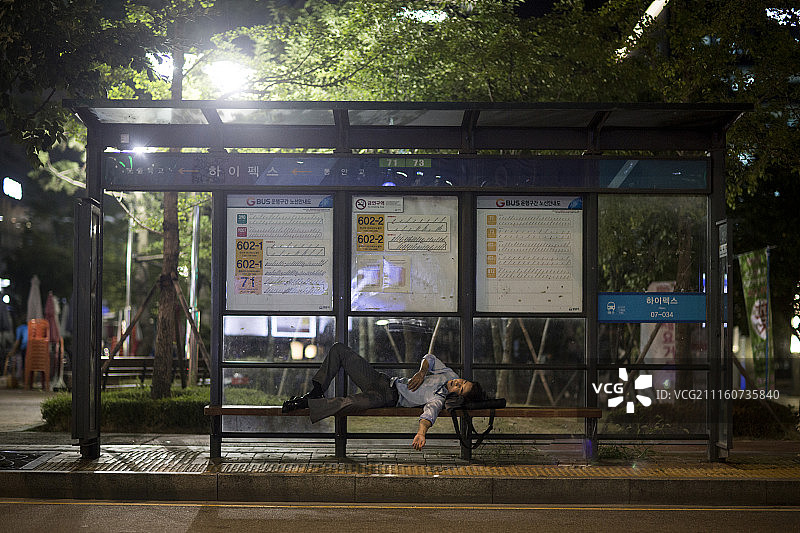 商人夜晚躺在巴士站长椅上摄影图片素材