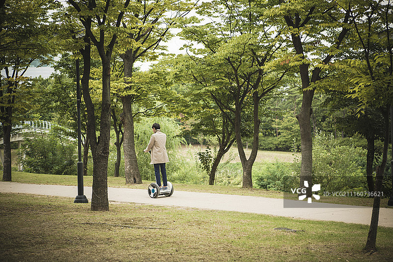 身穿风衣的男人在公园骑电动滑板车的摄影照片图片素材