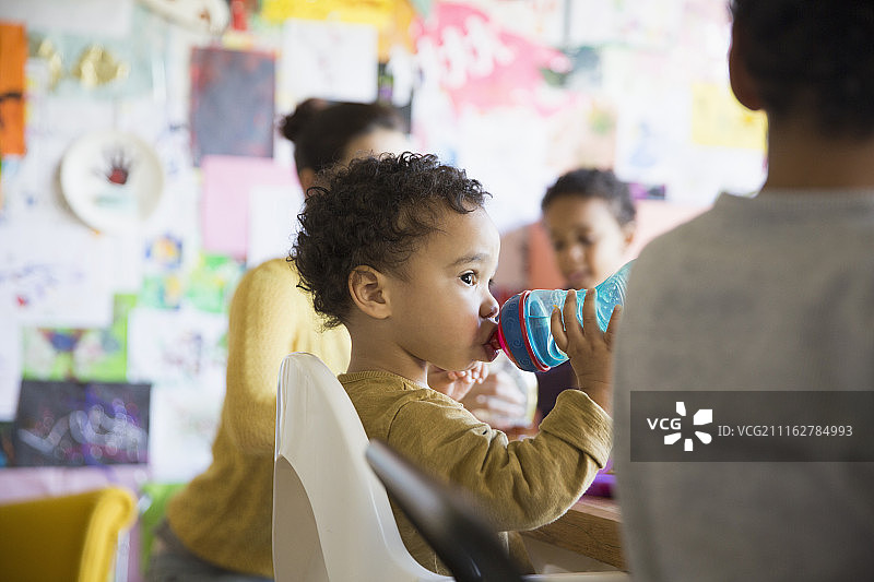 可爱的男婴在桌边用水杯喝水图片素材