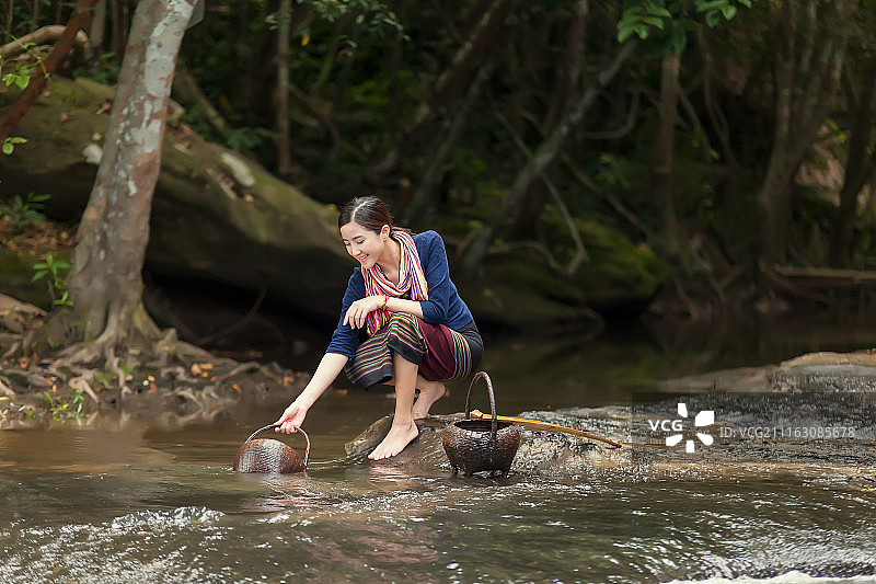 站在河中岩石上舀水的女人图片素材