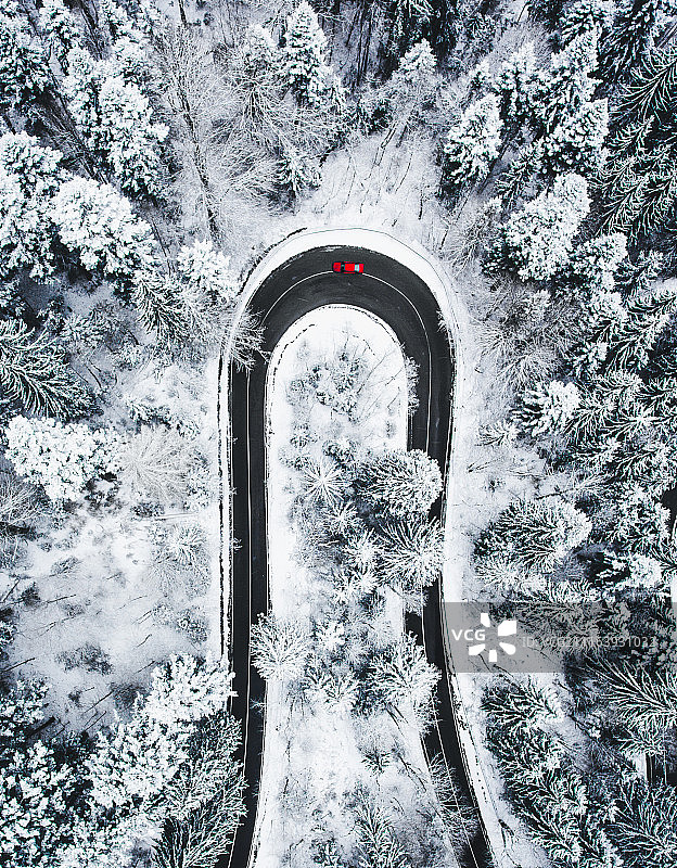 雪forest覆盖的森林中红色汽车在发夹弯道上行驶图片素材