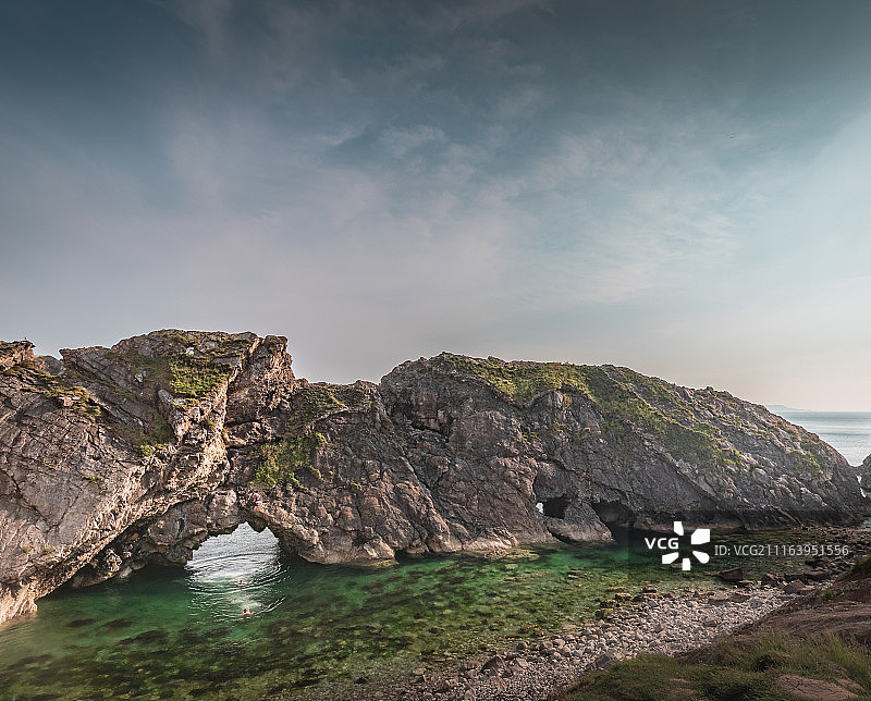 在有洞大岩石底部海中游泳的人们图片素材