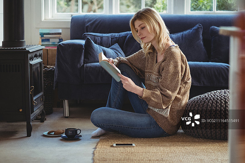 在客厅里一边喝茶一边读书的美丽女人图片素材