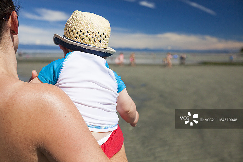 肩后视角看妈妈在沙滩上抱着男婴。图片素材
