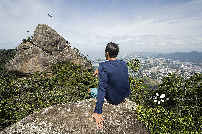 单身男子坐在巴西里约热内卢蒂如卡森林岩石上的背影图片素材