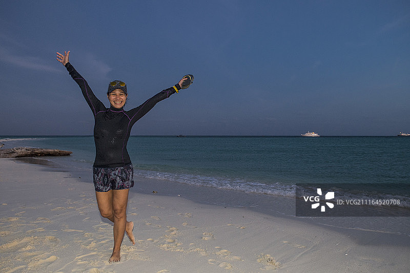 在日落海滩上手臂高举的微笑亚洲女性全身照图片素材