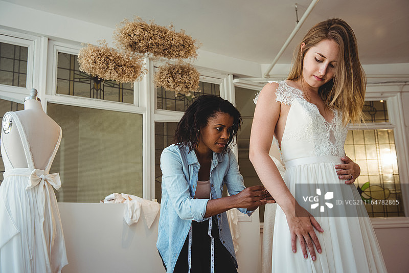 在时装设计师的帮助下，女子试穿婚纱图片素材
