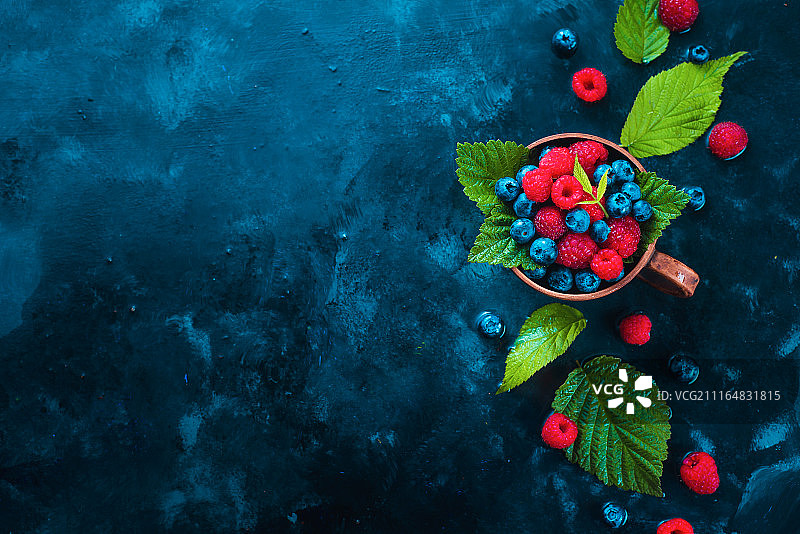 夏季浆果标题，陶瓷杯中覆盆子、蓝莓与绿叶图片素材