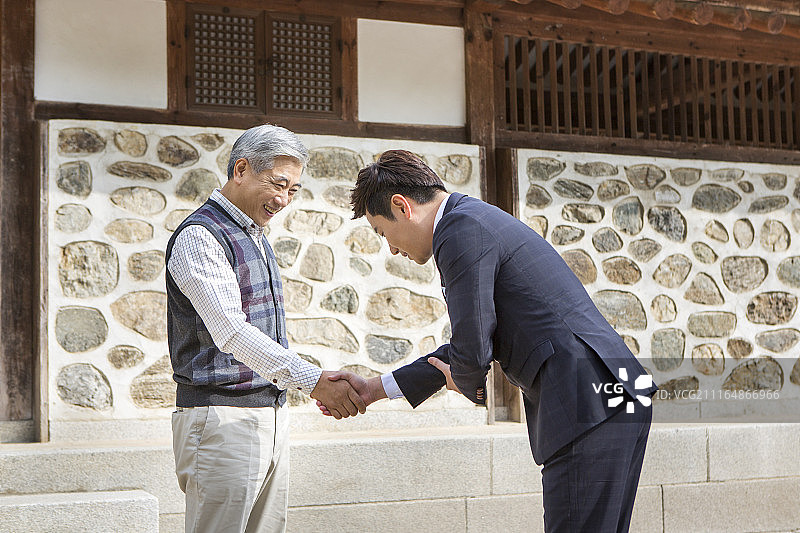 男人穿西装弯腰在传统韩屋前与年长的男人握手的摄影作品图片素材