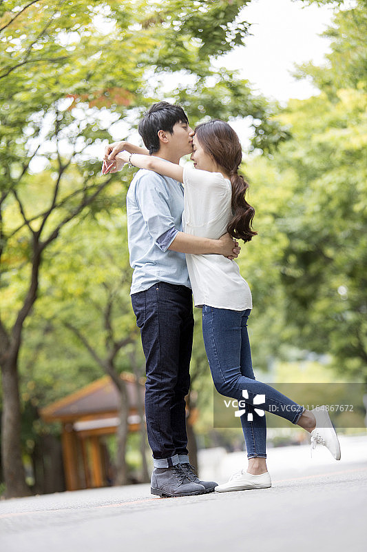 穿着休闲的情侣在公园街道上拥抱亲吻图片素材
