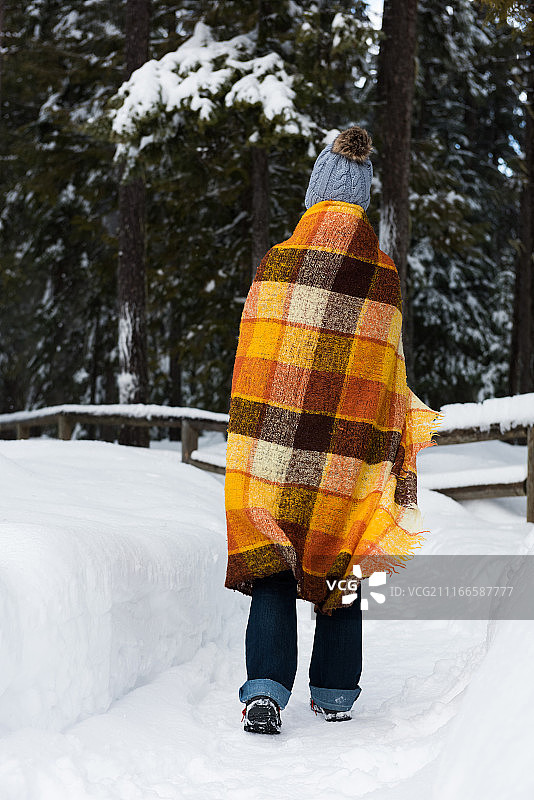 男人裹着毯子在雪地森林中行走图片素材