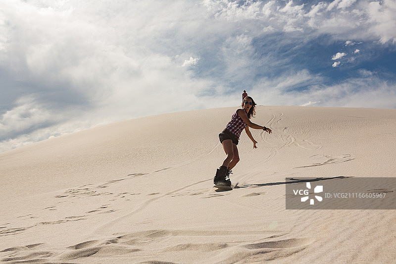 女人在沙丘上玩滑沙图片素材