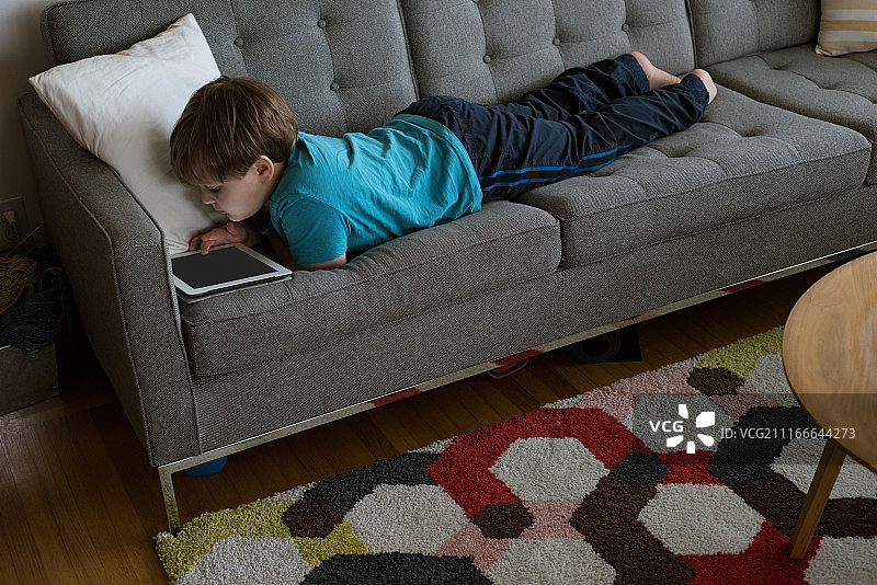 男孩躺在沙发上使用平板电脑的俯视图图片素材
