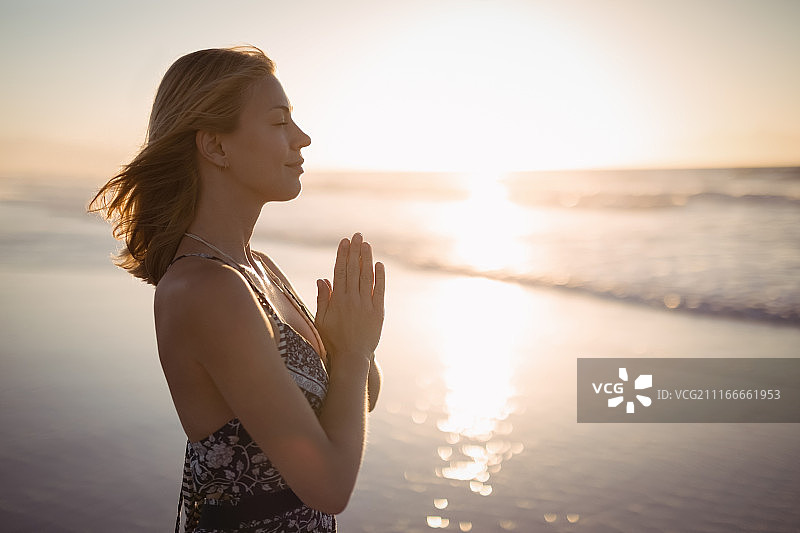 年轻女人在海滩上做瑜伽的侧视图图片素材