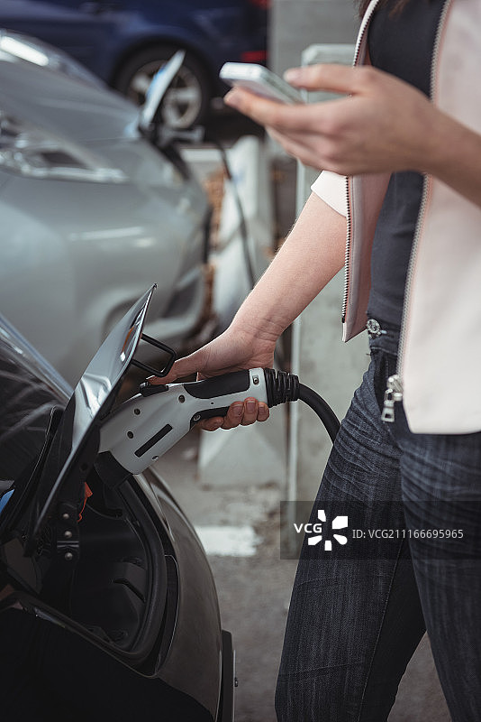 为电动汽车充电时使用手机的女人中段图片素材