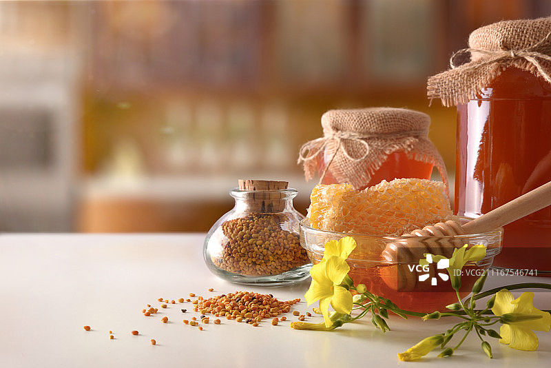 白色厨房桌上的蜂蜜罐、蜂巢和蜂花粉图片素材