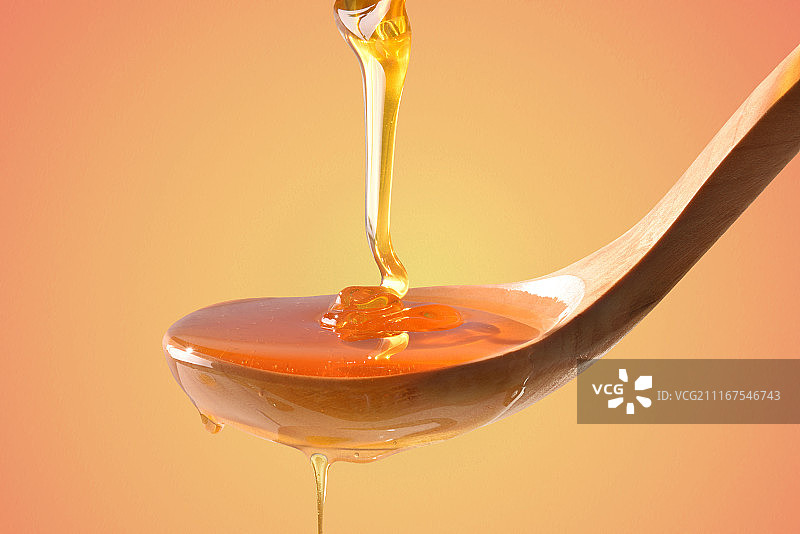 蜂蜜滴在橙色渐变背景的木勺上图片素材