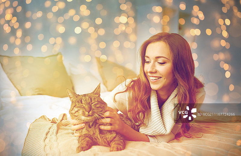 宠物、舒适、圣诞节、冬季和人物概念 - 快乐的年轻女子和猫躺在床上图片素材
