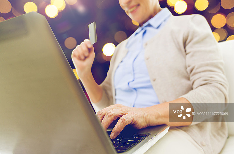 技术，年龄和人的概念-近距离年长妇女与笔记本电脑和信用卡或银行卡网上购物在圣诞节的灯光背景。有笔记本电脑和信用卡的资深女性图片素材