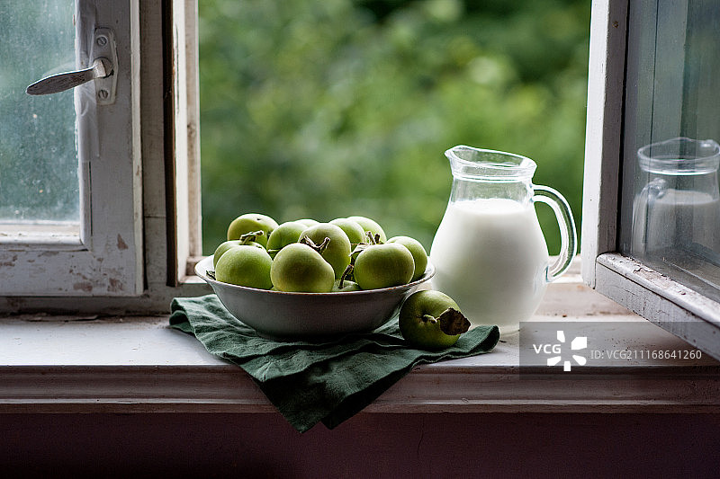 窗台上的牛奶壶和一碗苹果图片素材
