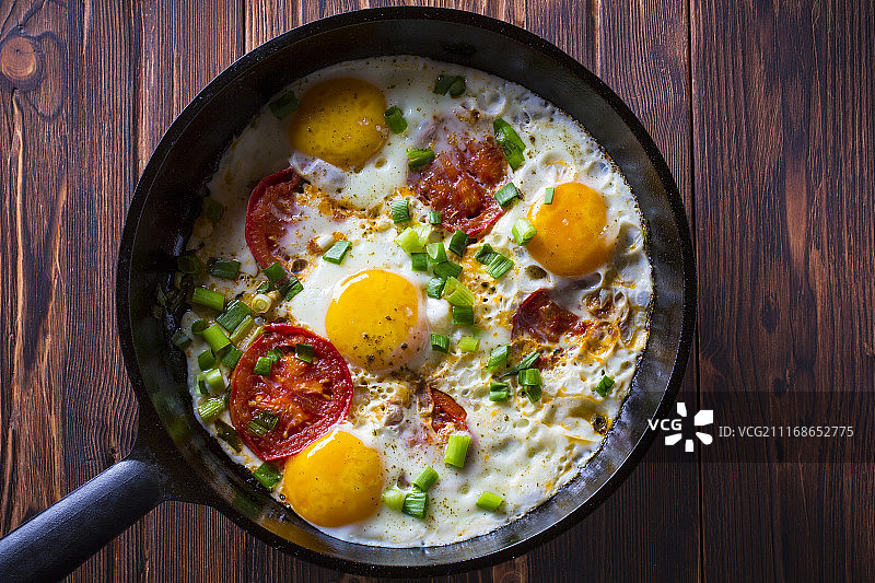 铸铁煎锅中的煎蛋和番茄，木质复古背景图片素材