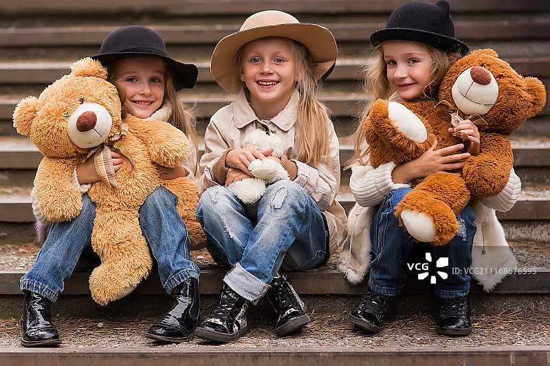 三个女孩坐在台阶上，手里拿着泰迪熊图片素材