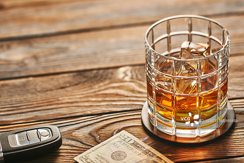 乡村木桌上放一杯威士忌或酒精饮料，带冰块和车钥匙，有复制空间。酒后驾车和酗酒概念。安全驾驶概念图片素材
