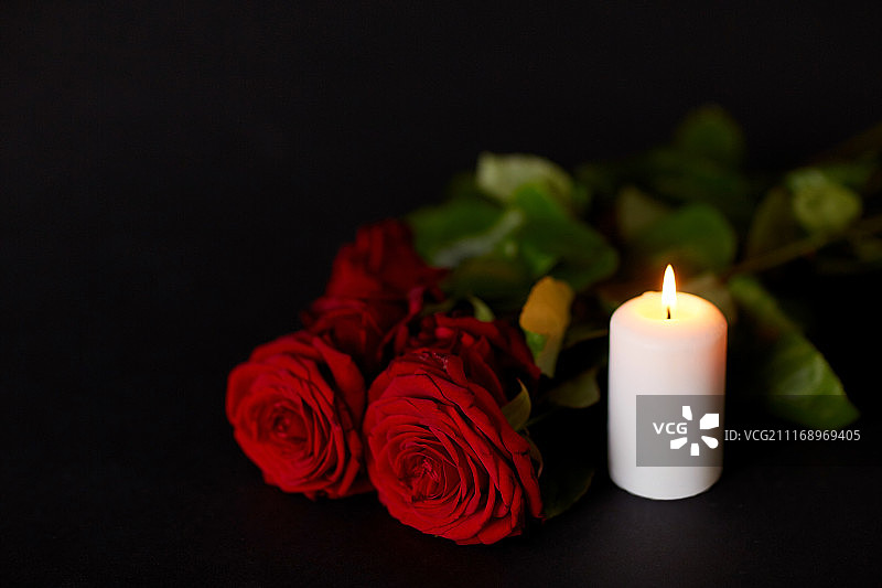 葬礼和哀悼概念-黑色背景上的红玫瑰和燃烧的蜡烛图片素材