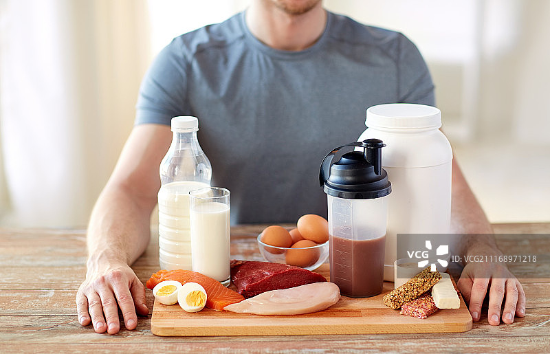 运动营养，健康饮食和人群概念 - 特写男性双手在木制砧板上拿着富含蛋白质的食物。桌子上富含蛋白质食物的男人特写图片素材