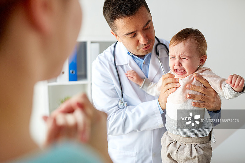 医疗、保健、儿科和人物概念——医生或儿科医生在诊所检查时抱着悲伤哭泣的女婴图片素材