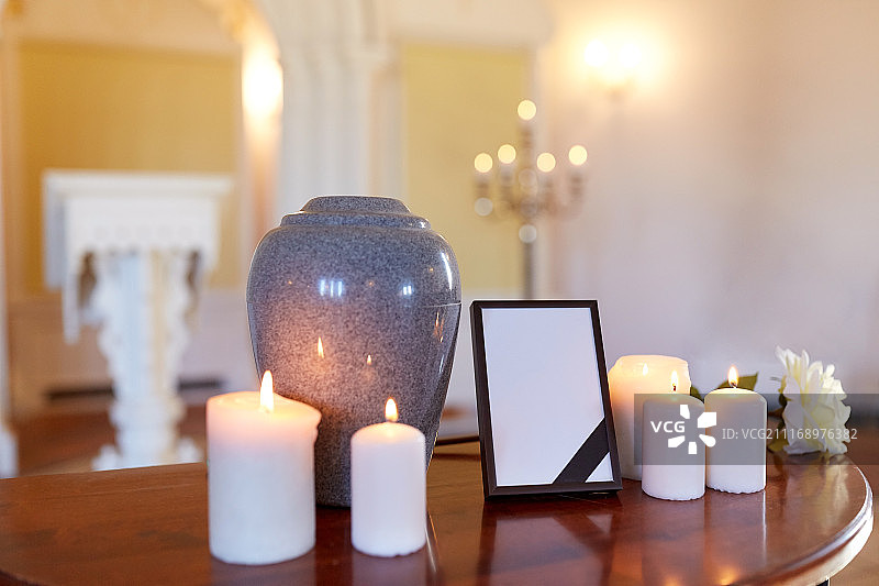 葬礼和哀悼概念——带黑色丝带的相框、火葬骨灰盒和教堂桌子上燃烧的蜡烛图片素材