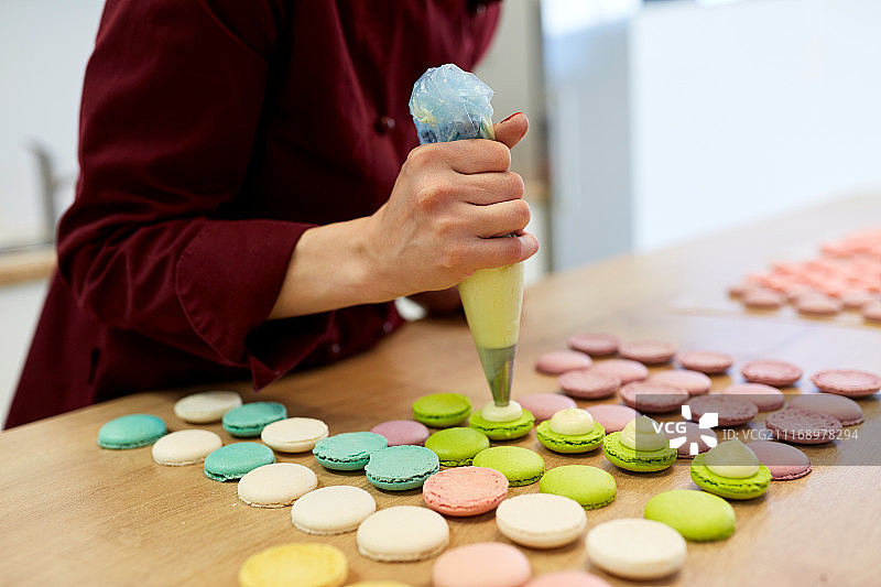 烹饪、食物和烘焙概念：厨师用糕点袋将奶油馅挤到糕点店的马卡龙外壳上图片素材