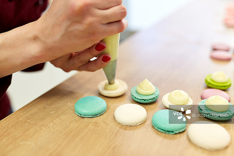 烹饪、食物和烘焙概念：厨师用糕点袋将奶油馅挤到糕点店的马卡龙外壳上图片素材