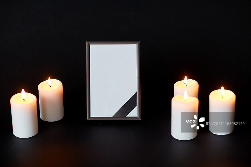 葬礼和哀悼概念——带缎带的空相框和黑色背景上的燃烧蜡烛，葬礼上的相框和蜡烛上的黑色缎带图片素材