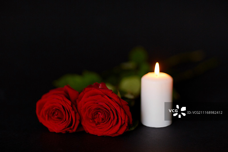 葬礼和哀悼概念-黑色背景上的红玫瑰和燃烧的蜡烛图片素材