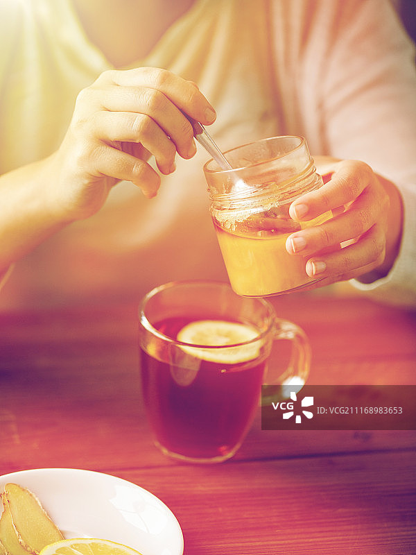 健康饮食理念：女性在茶杯中加入蜂蜜、柠檬和姜图片素材