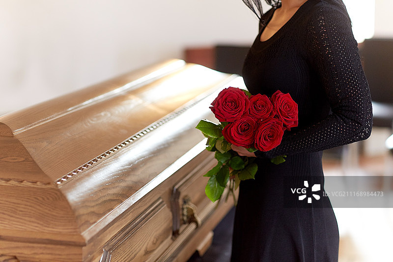 葬礼概念：拿着红玫瑰的女人和棺材图片素材