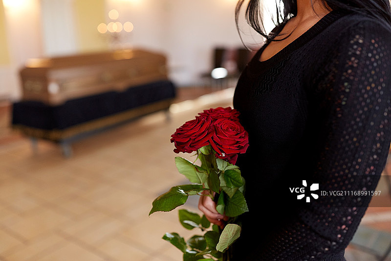 葬礼上的哀悼场景：女子手持红玫瑰，在教堂的棺材旁表达哀思图片素材