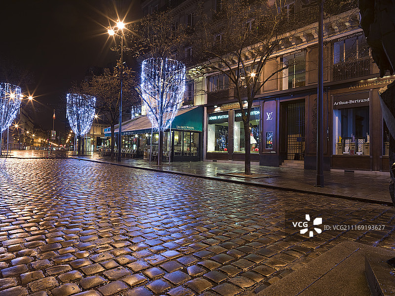 夜间鹅卵石路旁的照明树木和商店图片素材