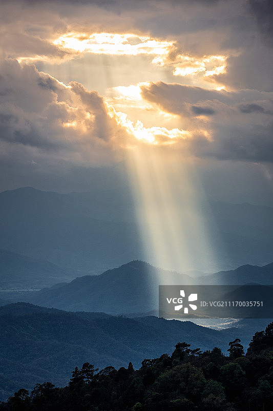 阳光穿过云洞照向黑暗的山脉图片素材