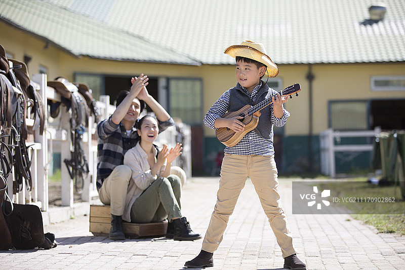 小男孩给父母弹奏尤克里里琴图片素材