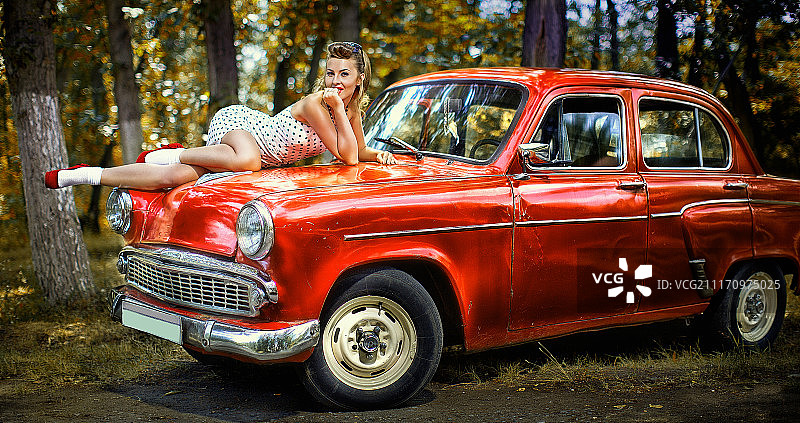 复古装扮的女人躺在红色老爷车引擎盖上图片素材