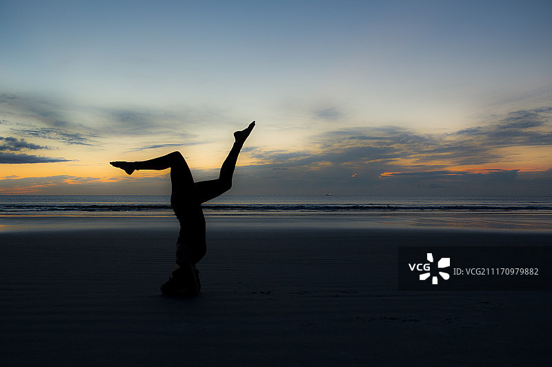 日落时在海滩上做瑜伽的女人轮廓图片素材
