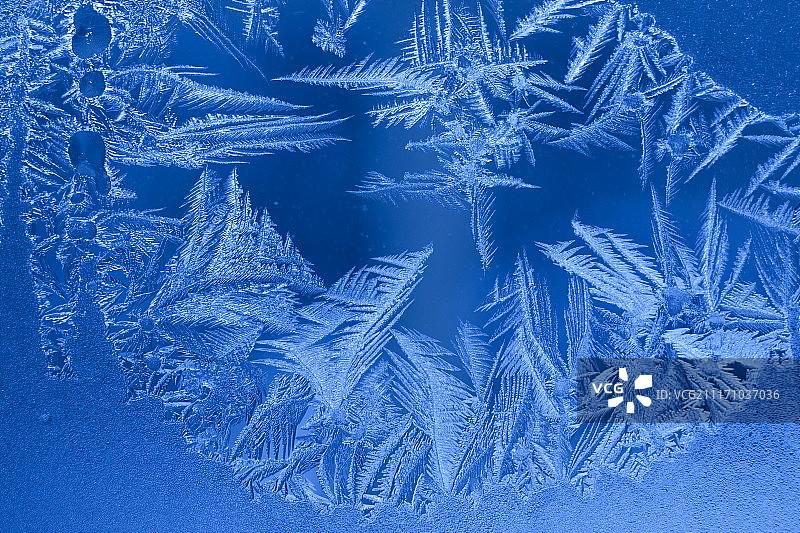 冬季窗户上尖锐雪花的蓝色冰霜图案图片素材