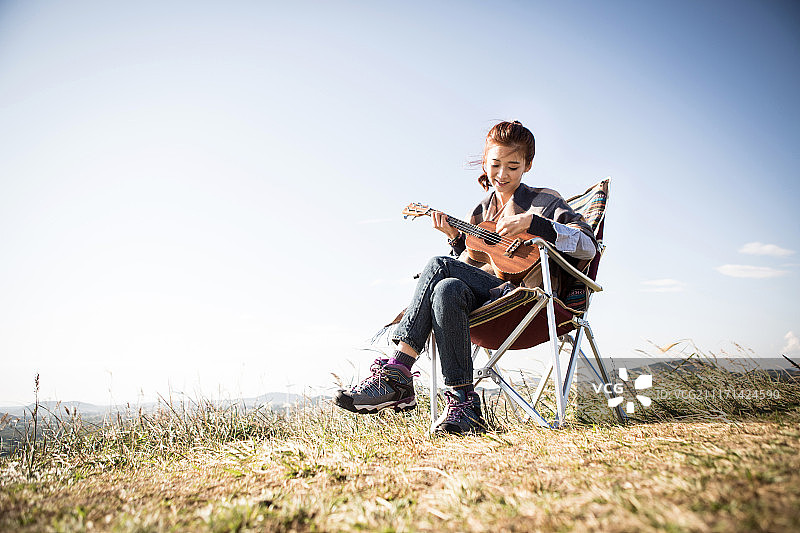 女人裹着毯子坐在山顶的椅子上弹吉他的摄影照片图片素材