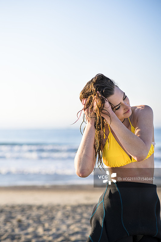 在海滩上穿着黄色比基尼，手放在头发上的女子半身照图片素材